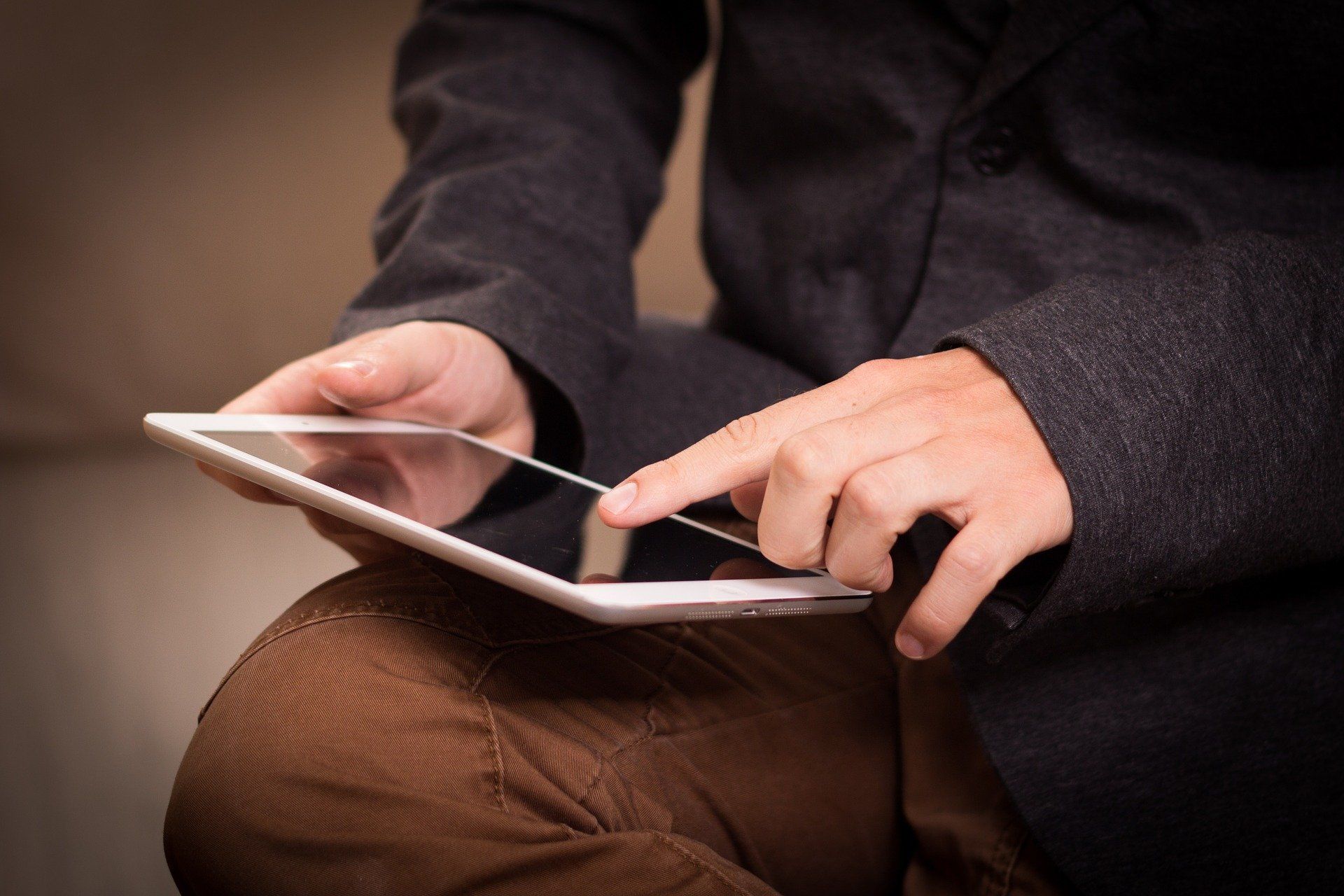 ein Mann hält ein Tablet auf seinen Knien und fährt mit dem Finger über den Bildschirm