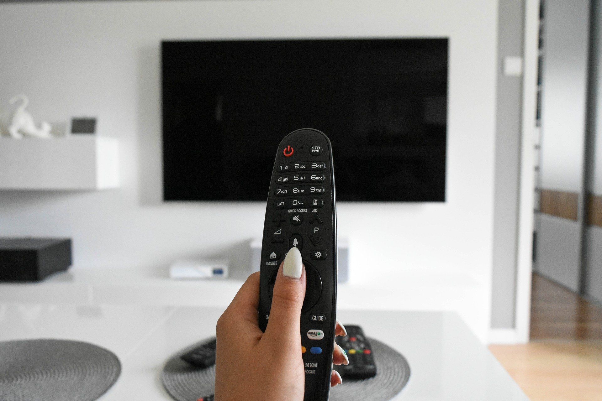 eine Hand mit einer Fernbedienung vor einem ausgeschalteten Fernseher