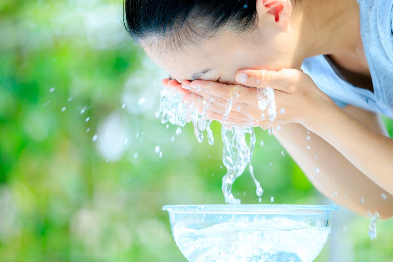 Frau erfrischt sich mit kühlendem Wasser und beugt Hitzestress vor