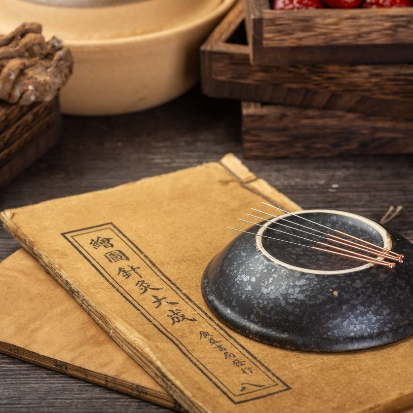 Akupunkturnadeln auf Unterteller mit chinesischer Schrift auf Heft