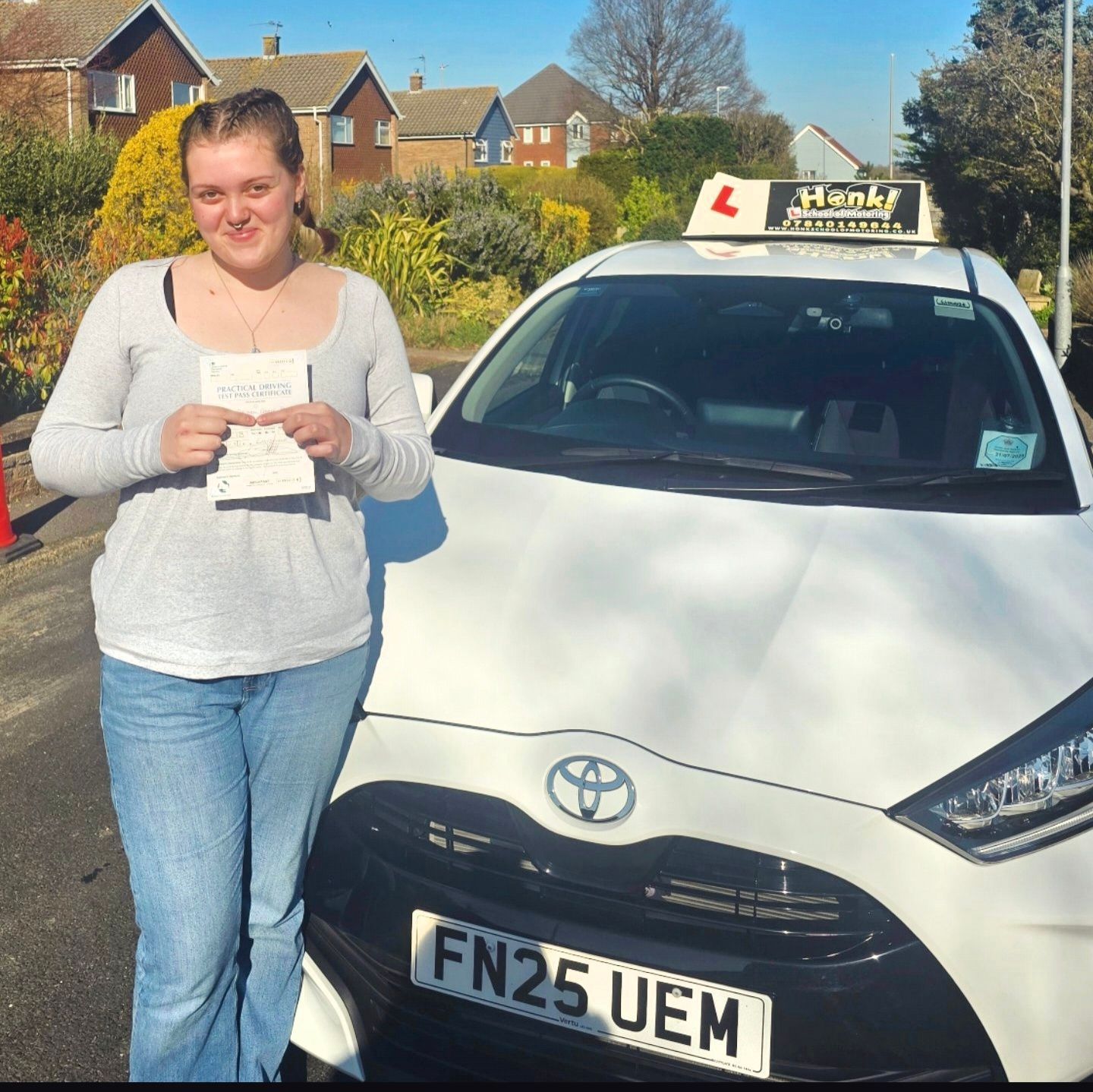 Happy pupil stands by car holding pass certificate.