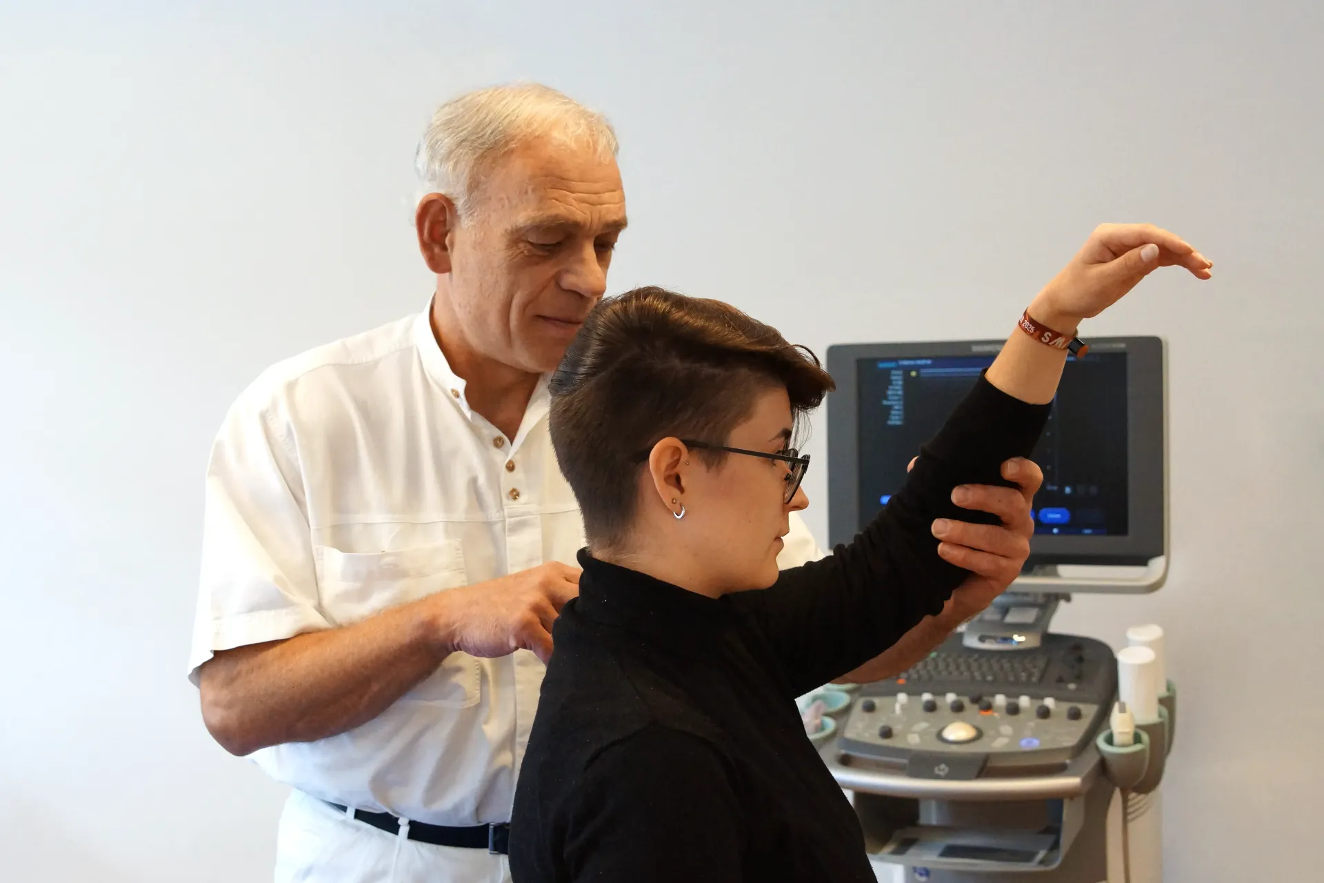 Dr. Becker untersucht den Schulterbereich einer Patientin