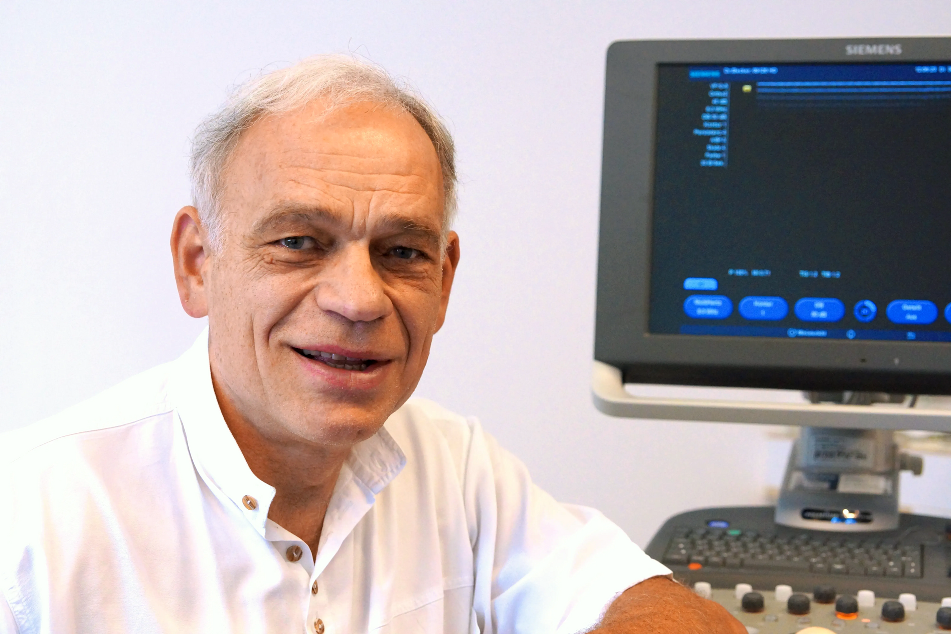 Portrait Dr. med. Christof Becker sitzend vor einem Analysebildschirm. Schaut freundlich in die Kamera