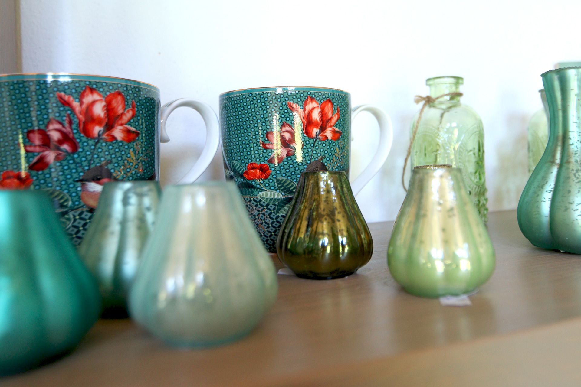 Tassen mit floralem Muster, kleine grüne Vasen im Hofladenregal