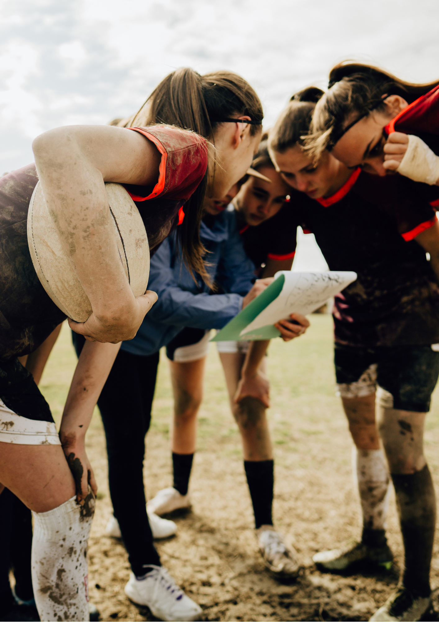 Femmes qui font du rugby réunies autour d'une coach qui donne des instructions en montrant un carnet