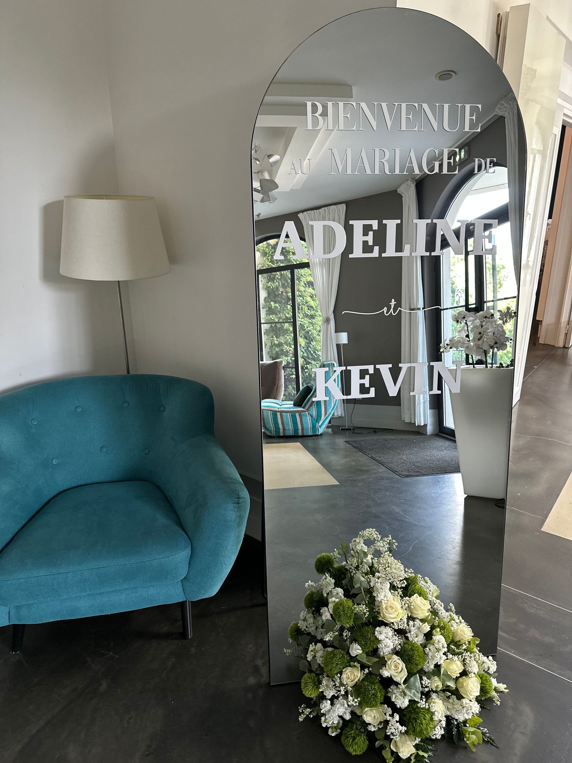 Un miroir reflétant une chaise bleue et des fleurs colorées disposées à côté.