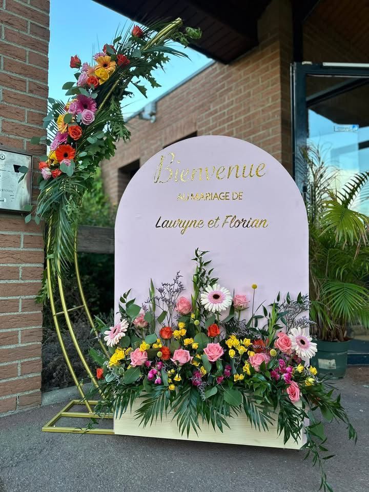 Arrangement floral sur une arche rose avec un panneau indiquant