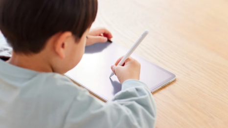 aufgeklappter Laptop aus dessen Monitor ein Stapel mit drei Büchern ragt auf dem ein roter Apfel liegt