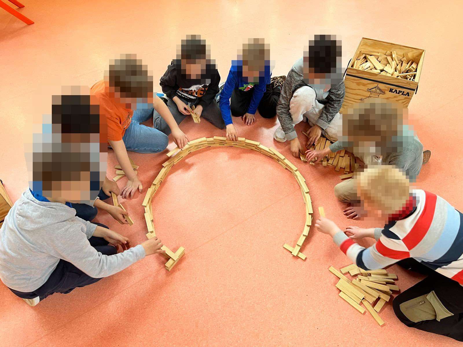 Kinder sitzen im Kreis und bauen mit Holzklötzen