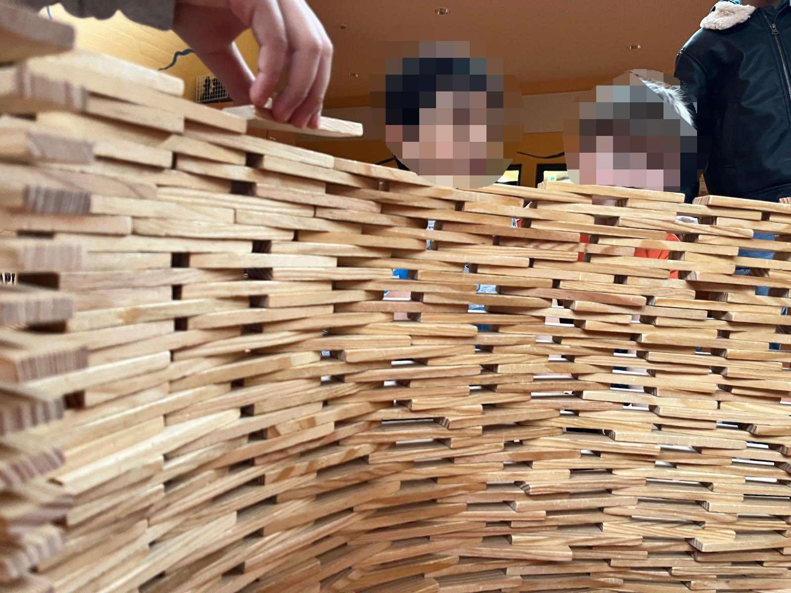 Kinder schauen über eine aus Holzklötzen gebaute Mauer
