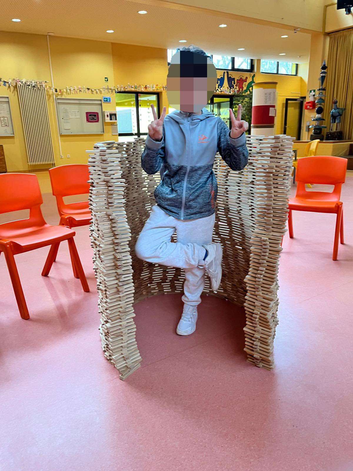 Kind steht in einer u-förmig gebauten Mauer aus Holzklötzen
