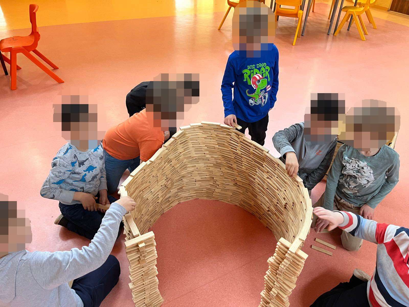 Kinder sitzen im Kreis und bauen eine Wand aus Holzklötzen