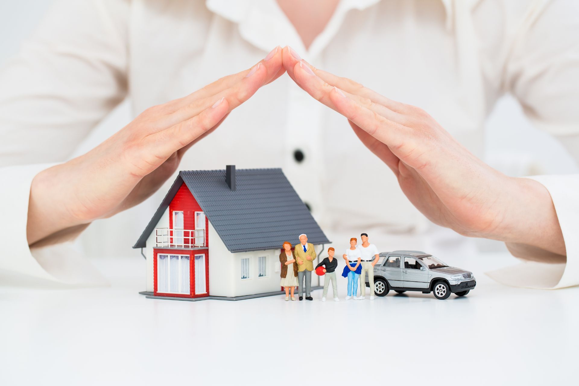 a person holding their hands over a model home and car