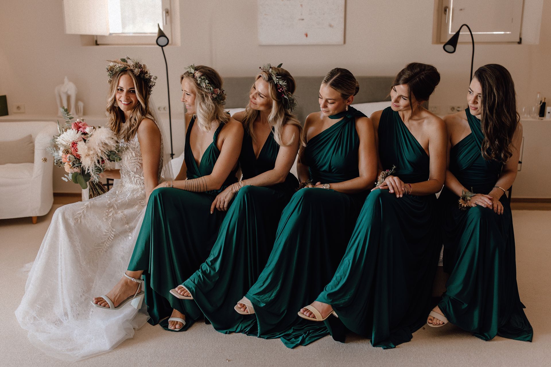 Auf dem Bett sitzend: Braut in Brautkleid mit ihren Brautjungfern, die alle das gleiche grüne Brautjungfernkleid tragen.