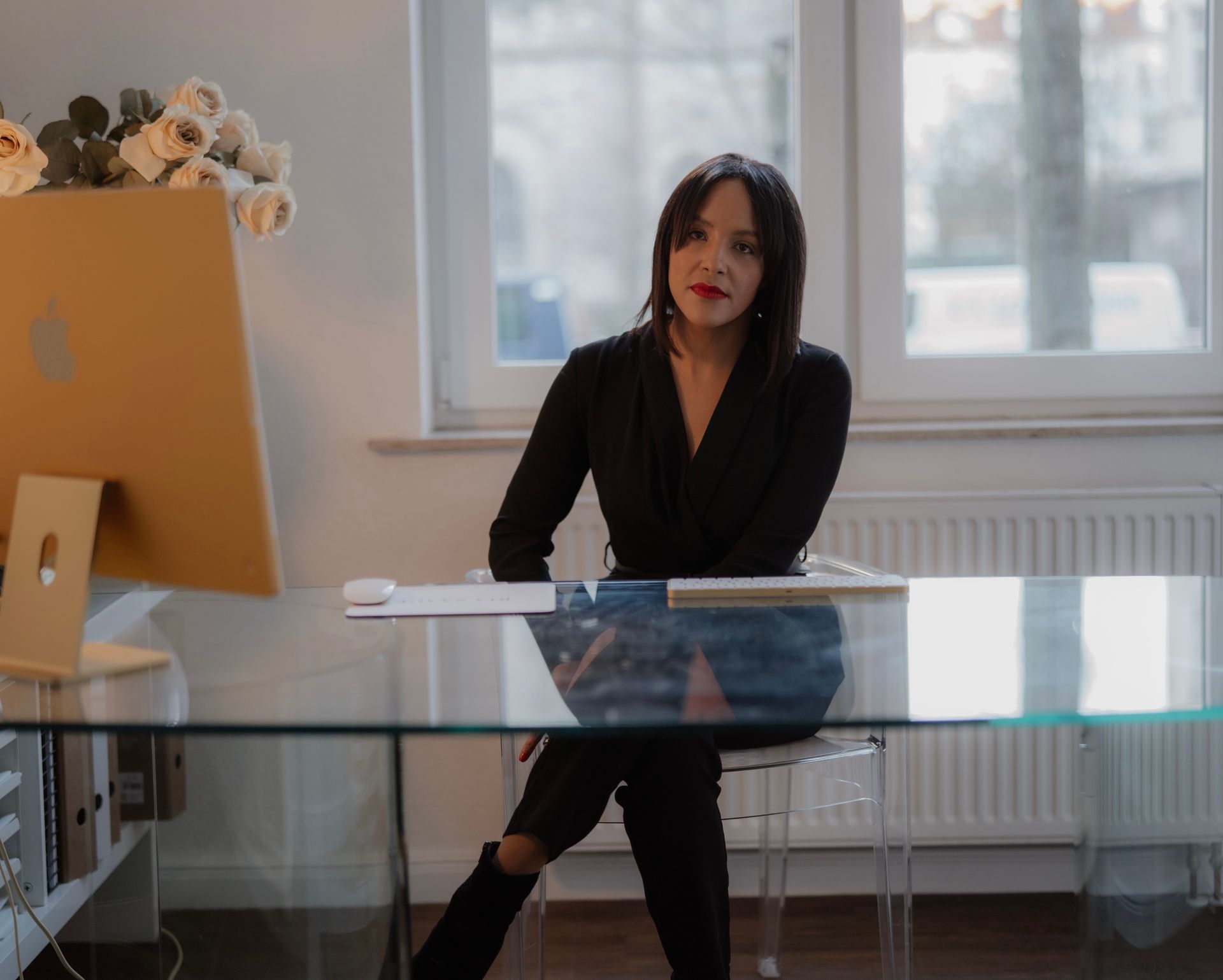 Die Brautstylistin Ria Saage sitzt an einem Schreibtisch und blickt in die Kamera. Sie trägt einen schwarzen Jumpsuit.