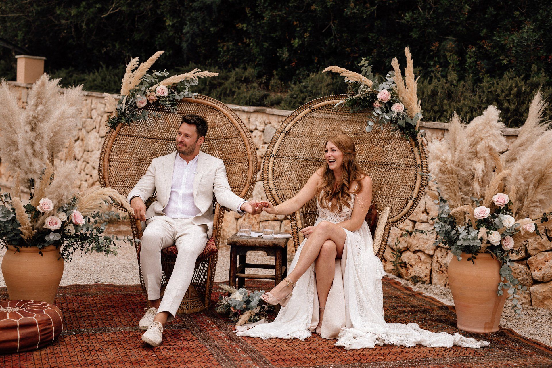 freie Trauung auf Finca in Mallorca, das Brautpaar sitzt in großen Korbsesseln, deren Lehnen mit frischen Blumen und Pampasgras geschmückt sind.