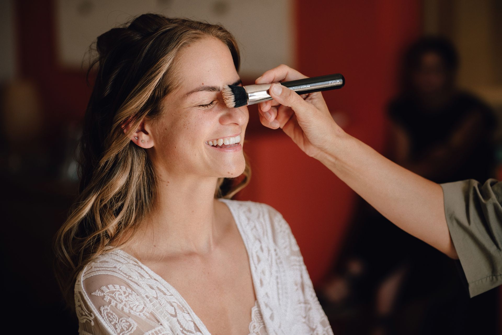Eine Braut wird beim Getting Ready von der Brautstylistin mit einem Pinsel abgepudert.