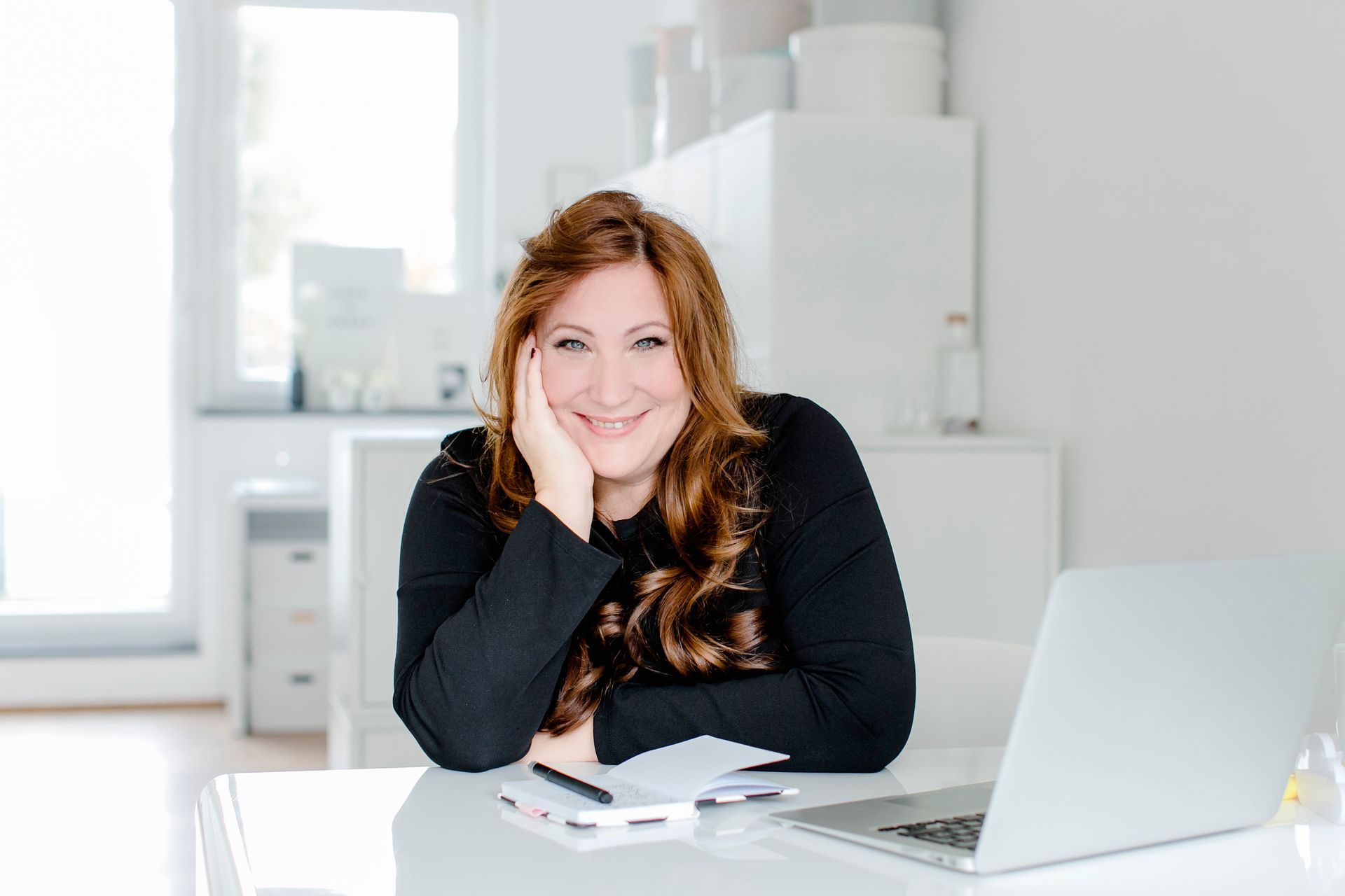 Hochzeitsplanerin Katrin Glaser strahlt in die Kamera. Sie sitzt am Schreibtisch, vor sich einen weißen Laptop.
