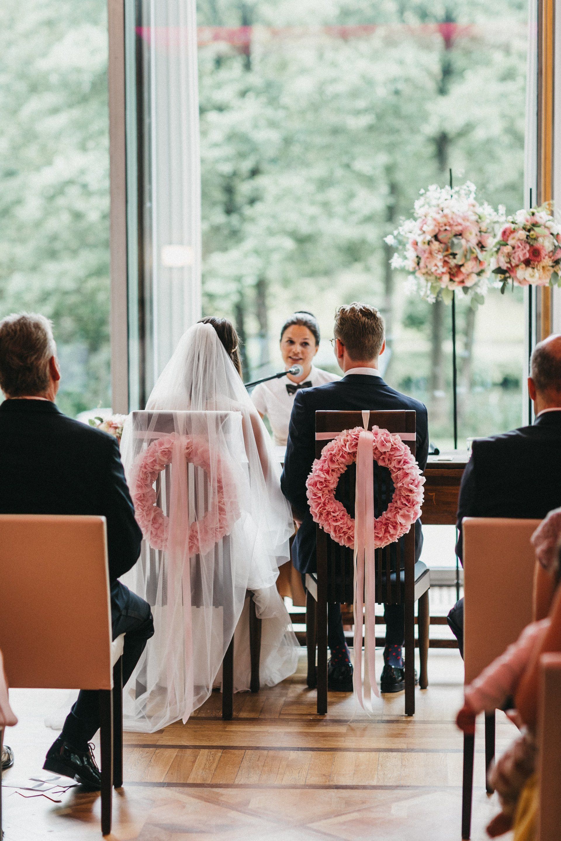 Freie Trauung in Hamburg: Die Stühle des Brautpaares sind mit rosafarbenen Hortensienkränzen geschmückt. Traurednerin spricht