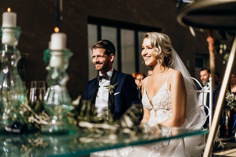 Es ist ein Brautpaar zu sehen, das während der freien Trauung strahlend vor der Freien Traurednerin Kristina Kutz sitzt.