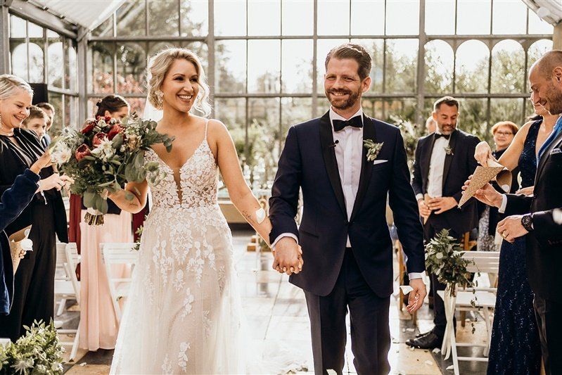 Brautpaar zieht aus einer hellen Orangerie nach der freien Trauung aus, hinten sieht man die Freie Traurednerin Kristina.
